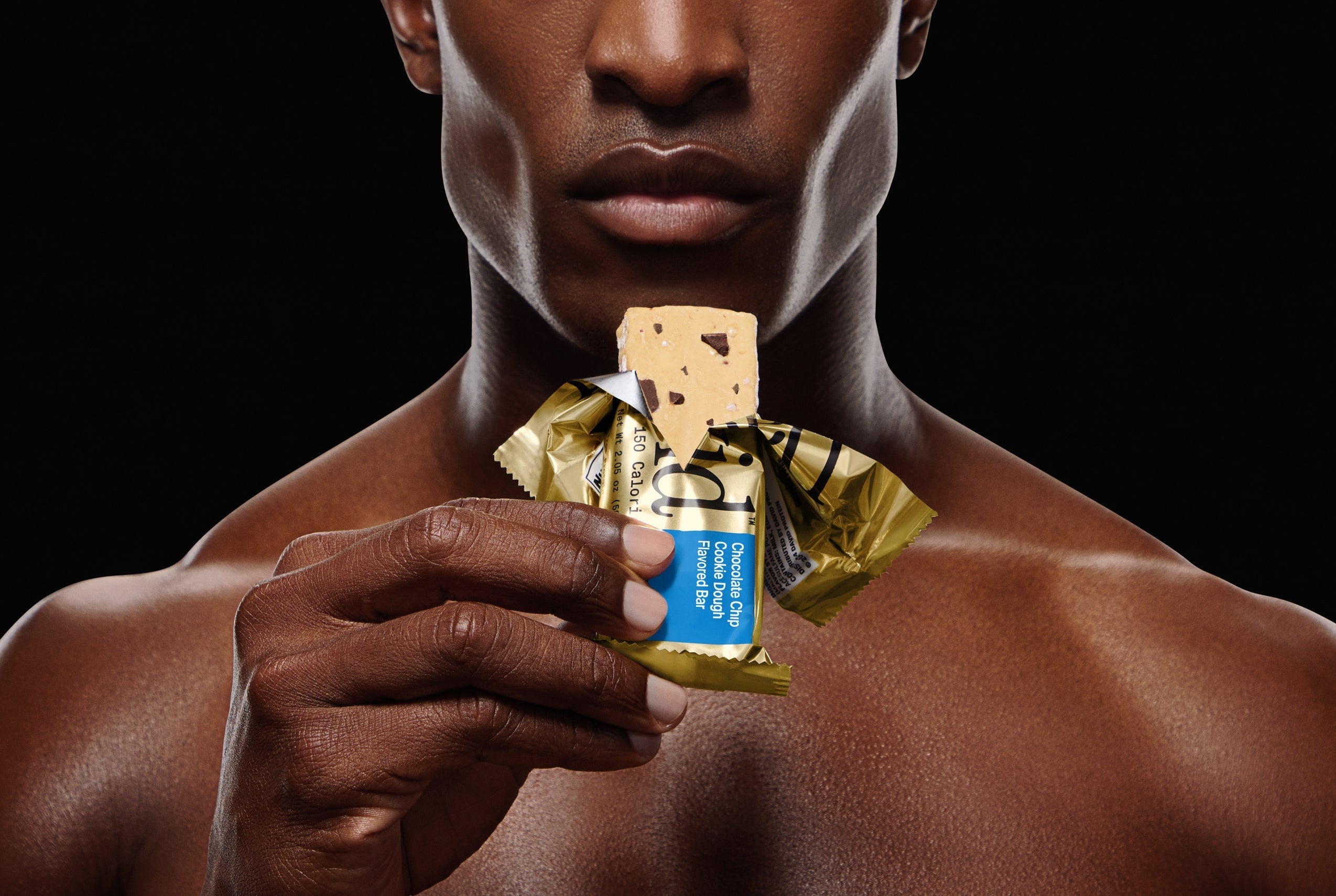 Man holding a Chocolate Chip Cookie Dough protein bar against a black background